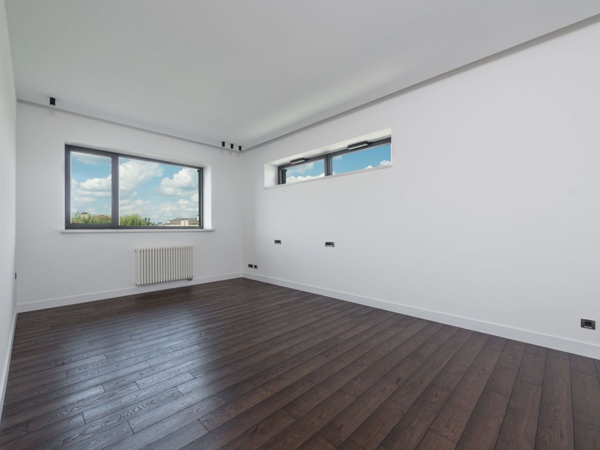 An empty, freshly cleaned apartment room with wood flooring and bright windows